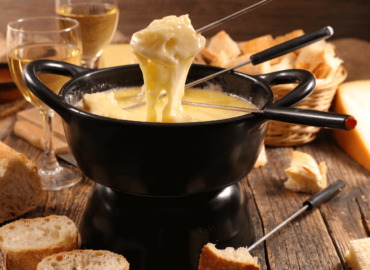 Fondue Cheese (melted cheese) in the traditional Swiss style, in a big pot with utensils for dipping of appetizers and finger foods