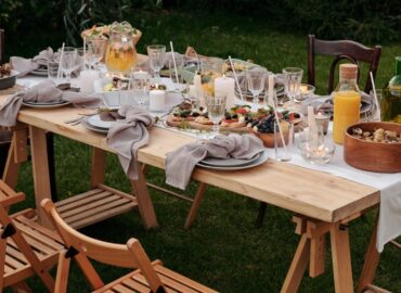 An outdoor picnic spread with cheese, fruits, and meat.